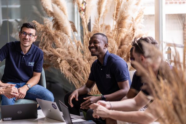 Antoine Doison et William Kaboré, 2 experts cybersécurité chez SKillX assis avec 2 autres collègues qu'on ne distingue pas complètement car cachés par des fleurs de pampa. Assis tous les 4, ils sourient.